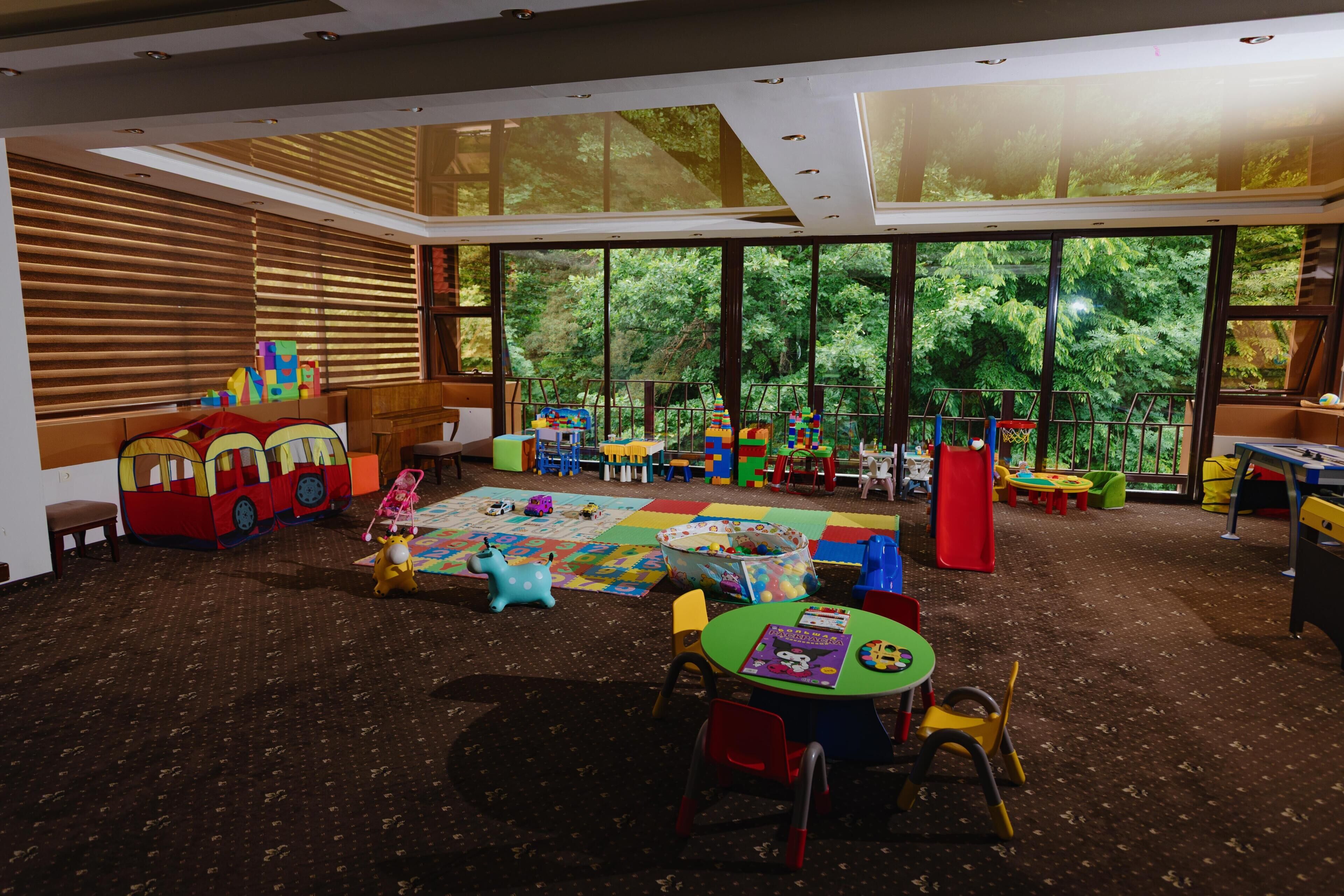 A spacious children's playroom with large windows, a variety of play structures, and a carpeted floor.