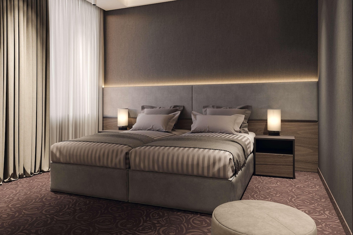 Una habitación de hotel moderna con una cama grande, dos mesitas de noche y un cabecero con iluminación integrada.
