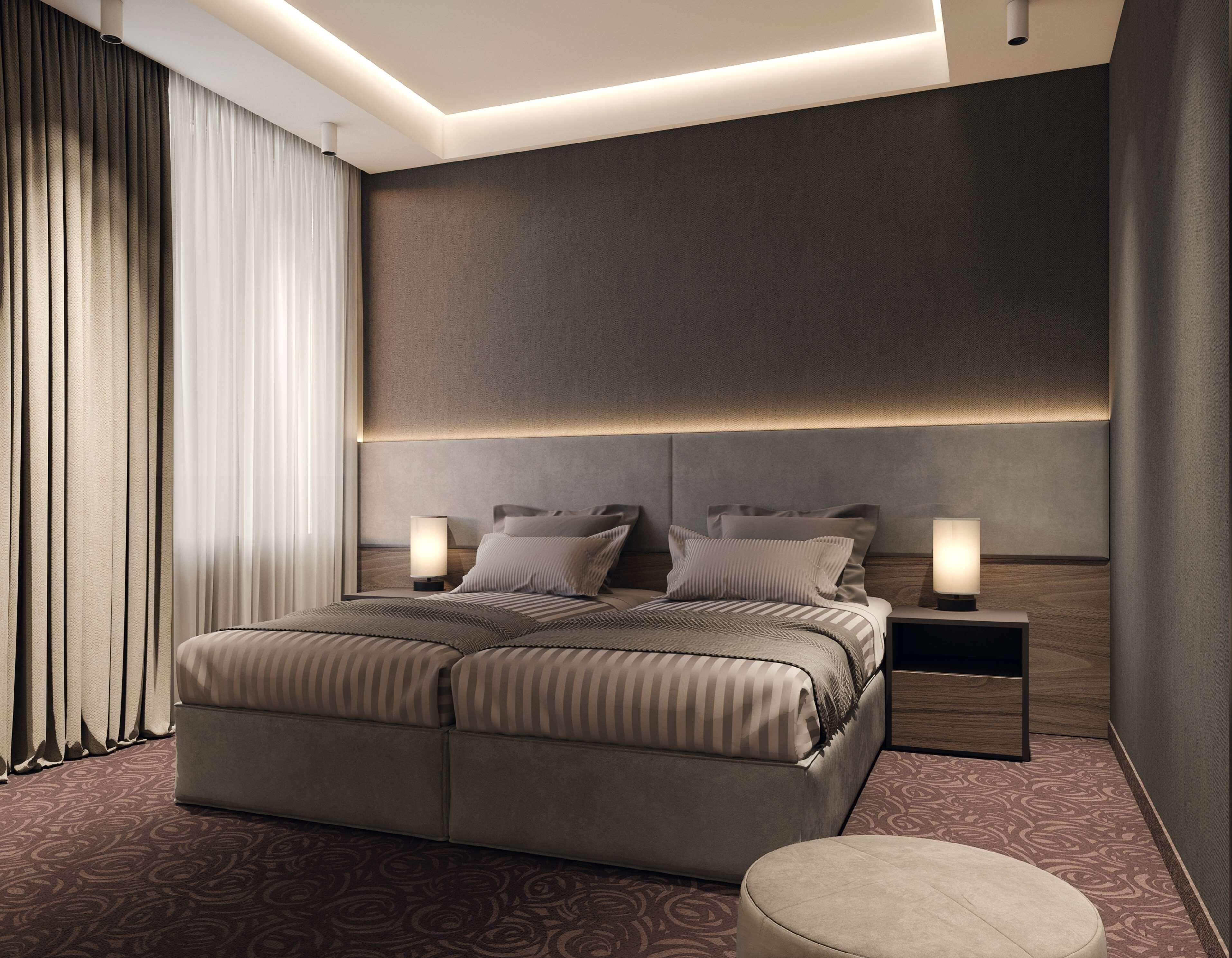 Una habitación de hotel moderna con una cama grande, dos mesitas de noche y un cabecero con iluminación integrada.