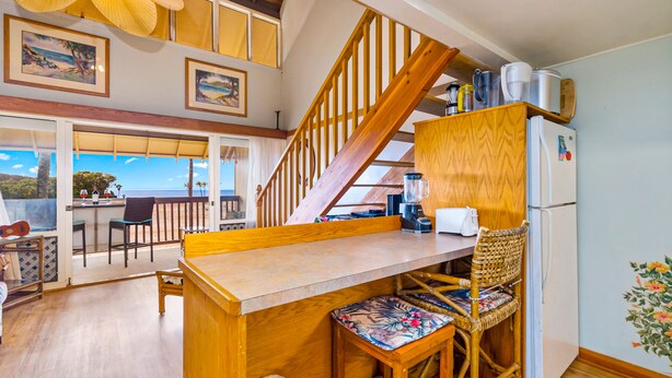 A kitchen with wooden stools, a wooden counter, and a view of the ocean. - Kepuhi Beach Resort (Maunaloa)