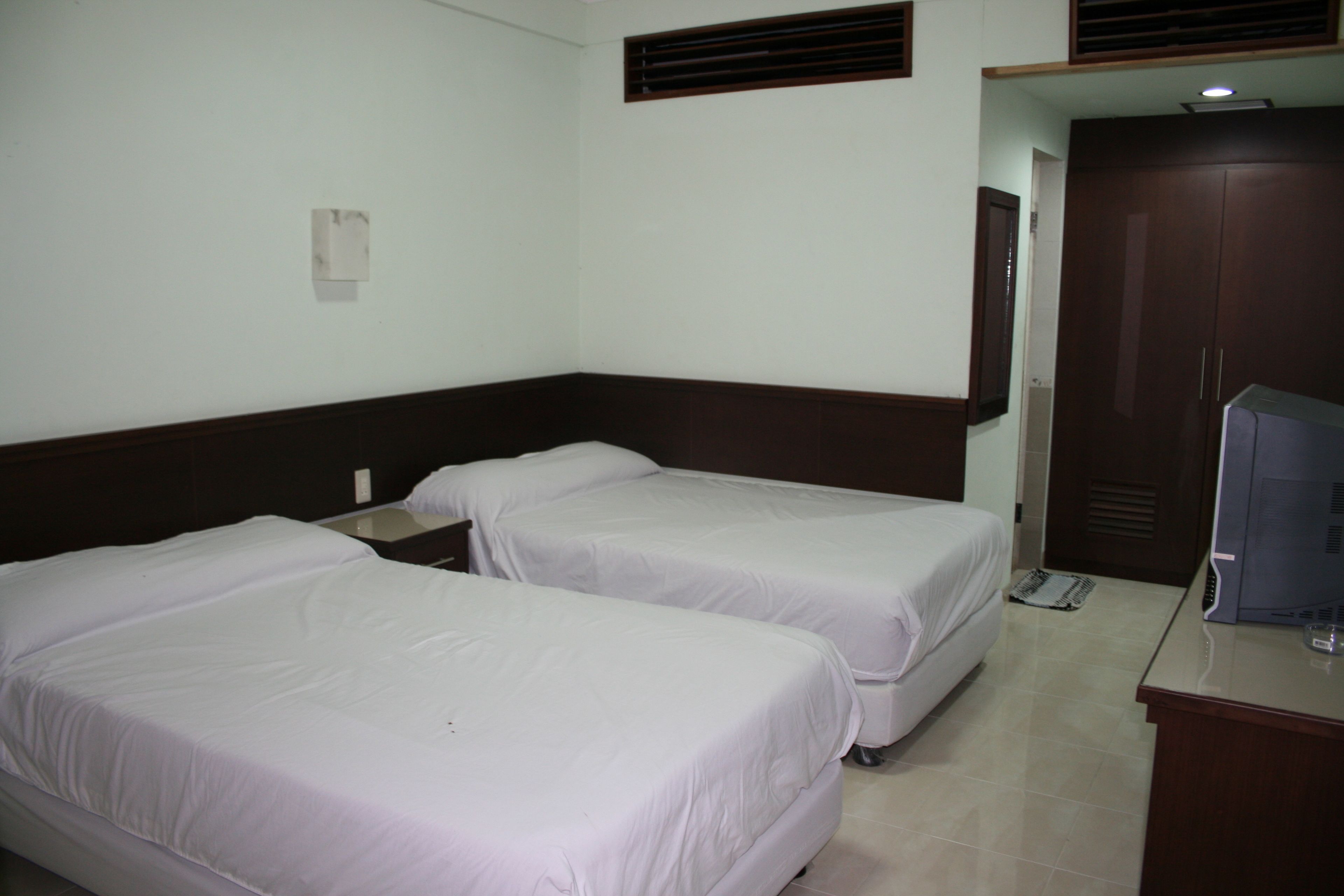 A hotel room with two single beds, a desk with a computer, and a wardrobe.