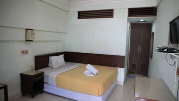 A hotel room with a bed, a nightstand, a desk, a television, and a door.