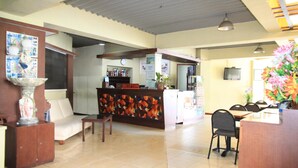 Un espace d’accueil comprenant un comptoir de réception, un canapé, une table à manger avec des chaises et une plante décorative.