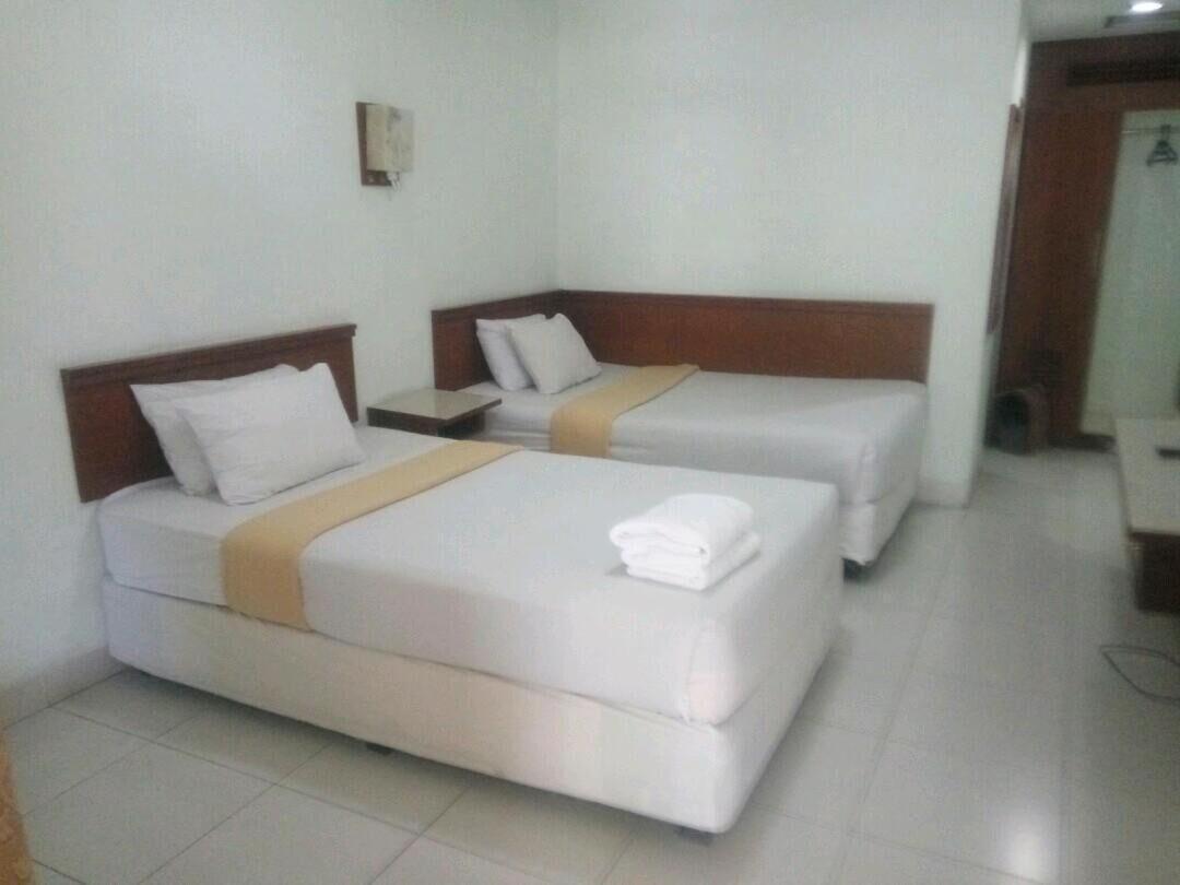 A hotel room with two beds, each with a wooden headboard, white bedding, and a beige blanket.