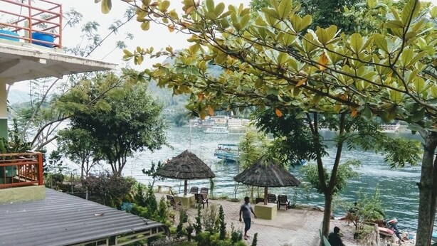 Une terrasse au bord de la rivière, agrémentée de parasols en chaume, de sièges et de plantes en pot.