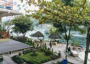 Een terras aan de rivier met rieten parasols, zitplaatsen en potplanten.