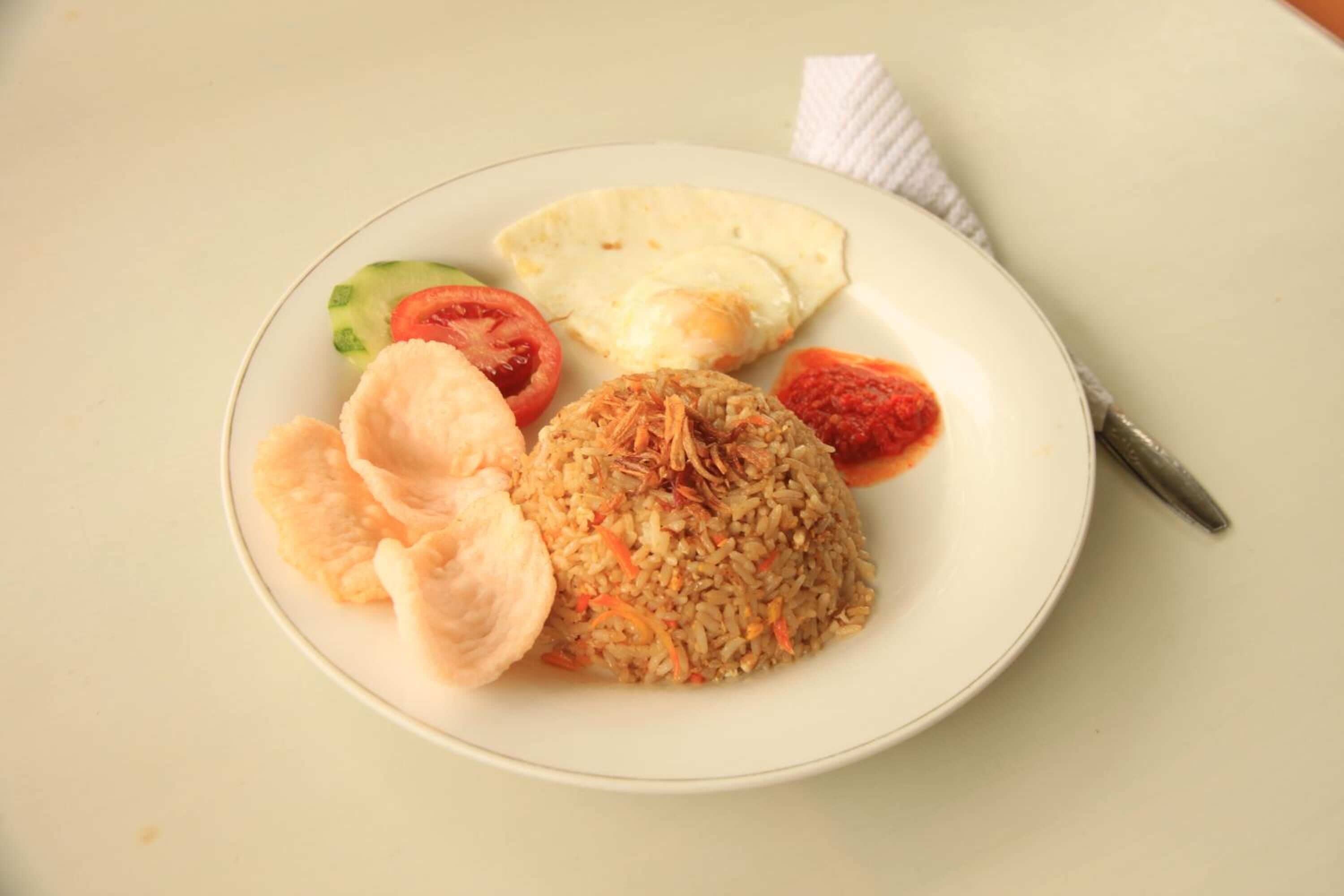 A plate with rice, vegetables, and a piece of bread on a white table.