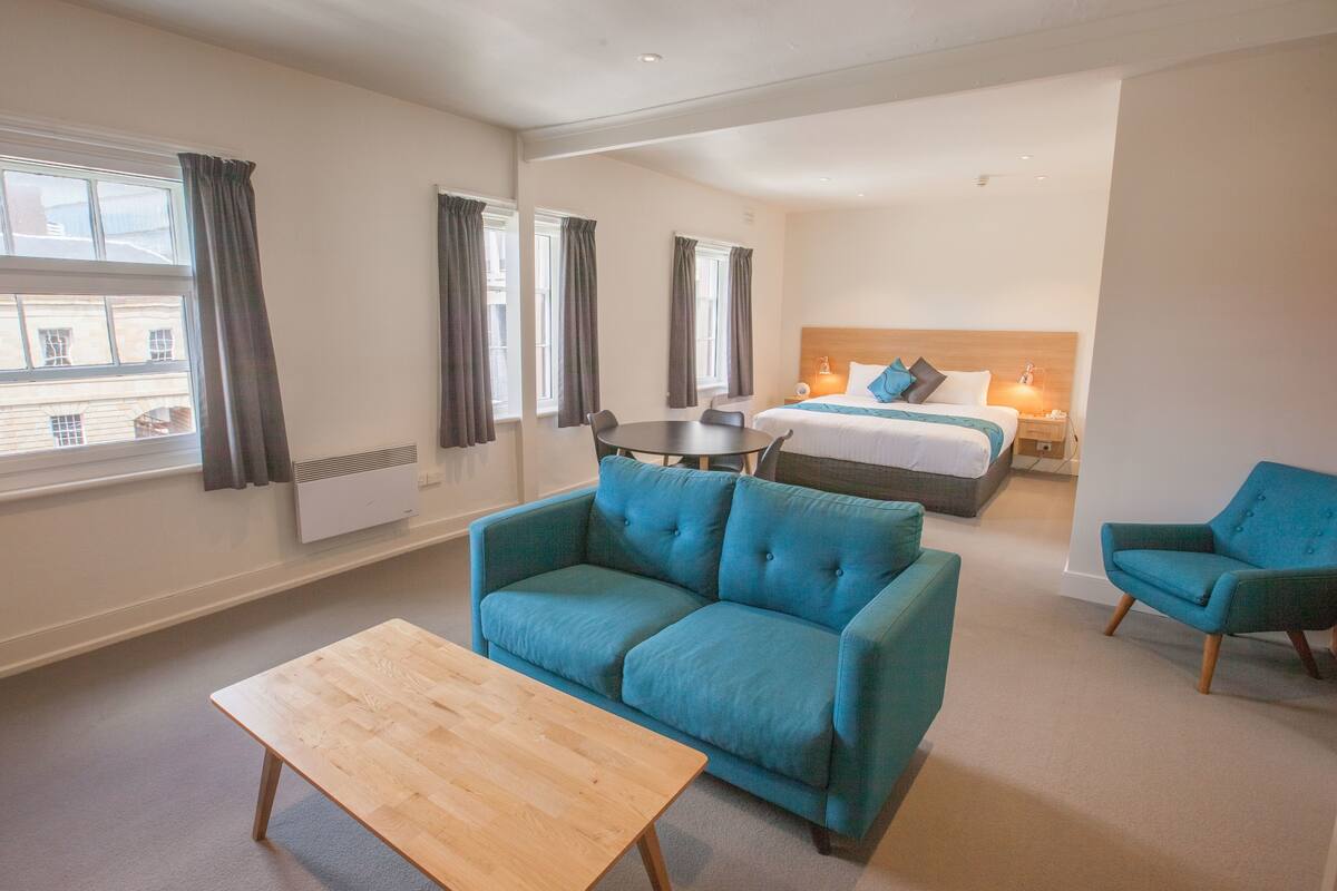 A hotel room with a bed, a blue sofa, a wooden table, and a chair.