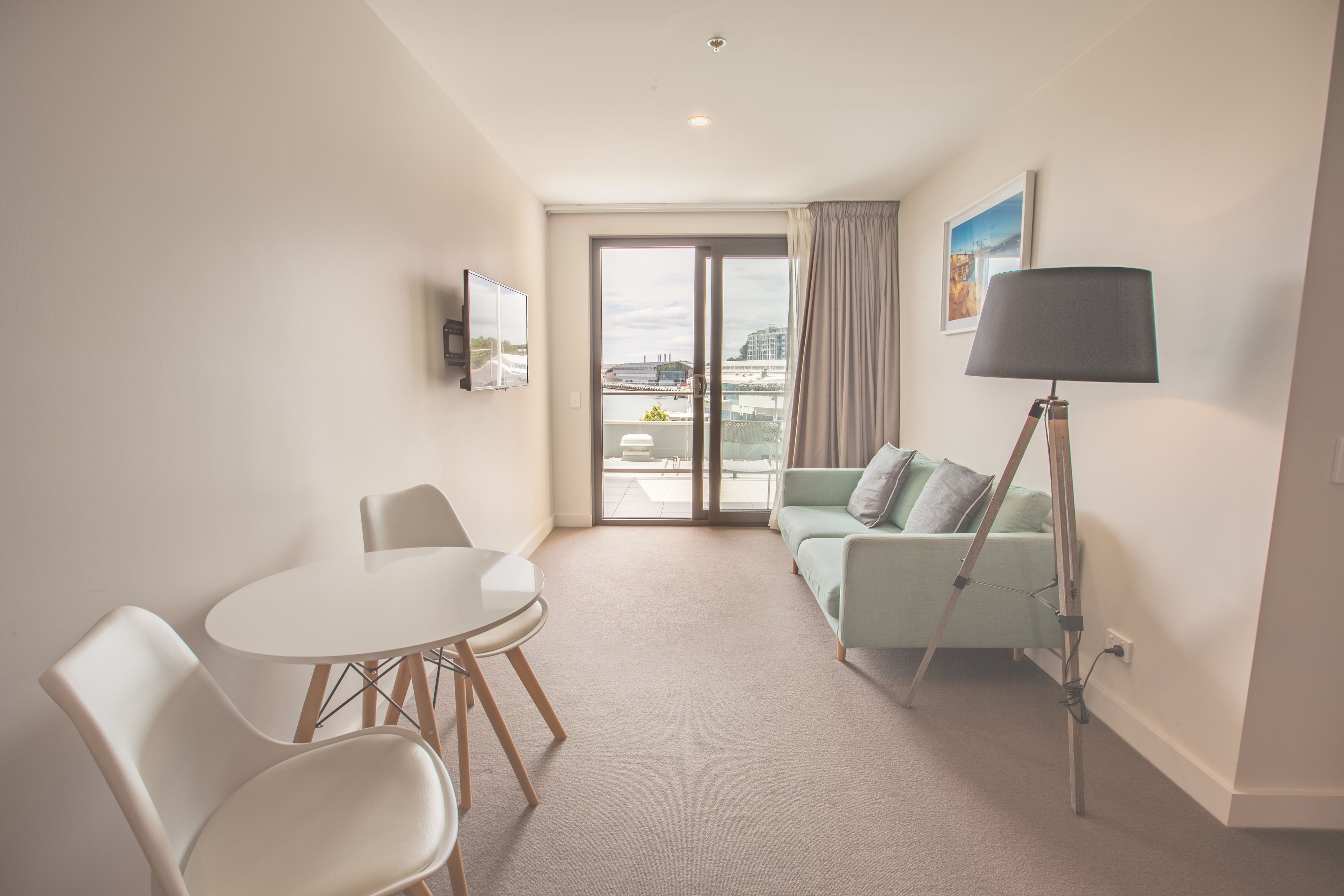Una habitación de hotel moderna con balcón, un área de comedor con mesa y sillas, un sofá y una lámpara de pie.