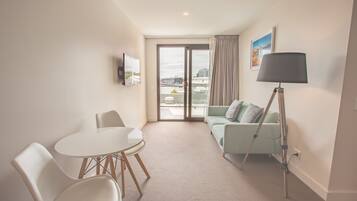 Una habitación de hotel moderna con balcón, un área de comedor con mesa y sillas, un sofá y una lámpara de pie.