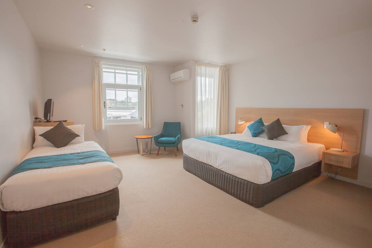 A hotel room with two beds, a chair, a small table, and a nightstand with a lamp.