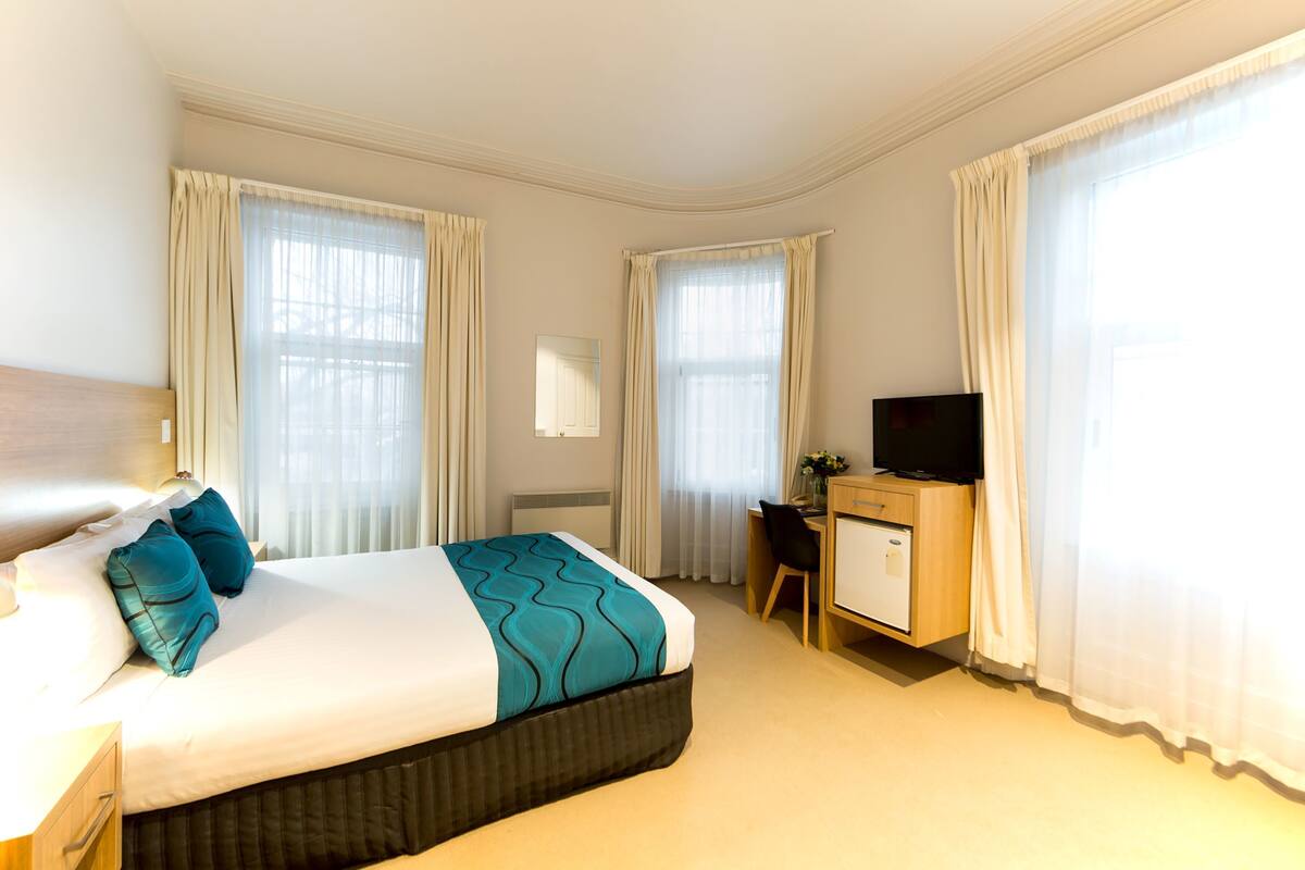 A hotel room with a bed, a desk, a chair, a television, and a window with curtains.