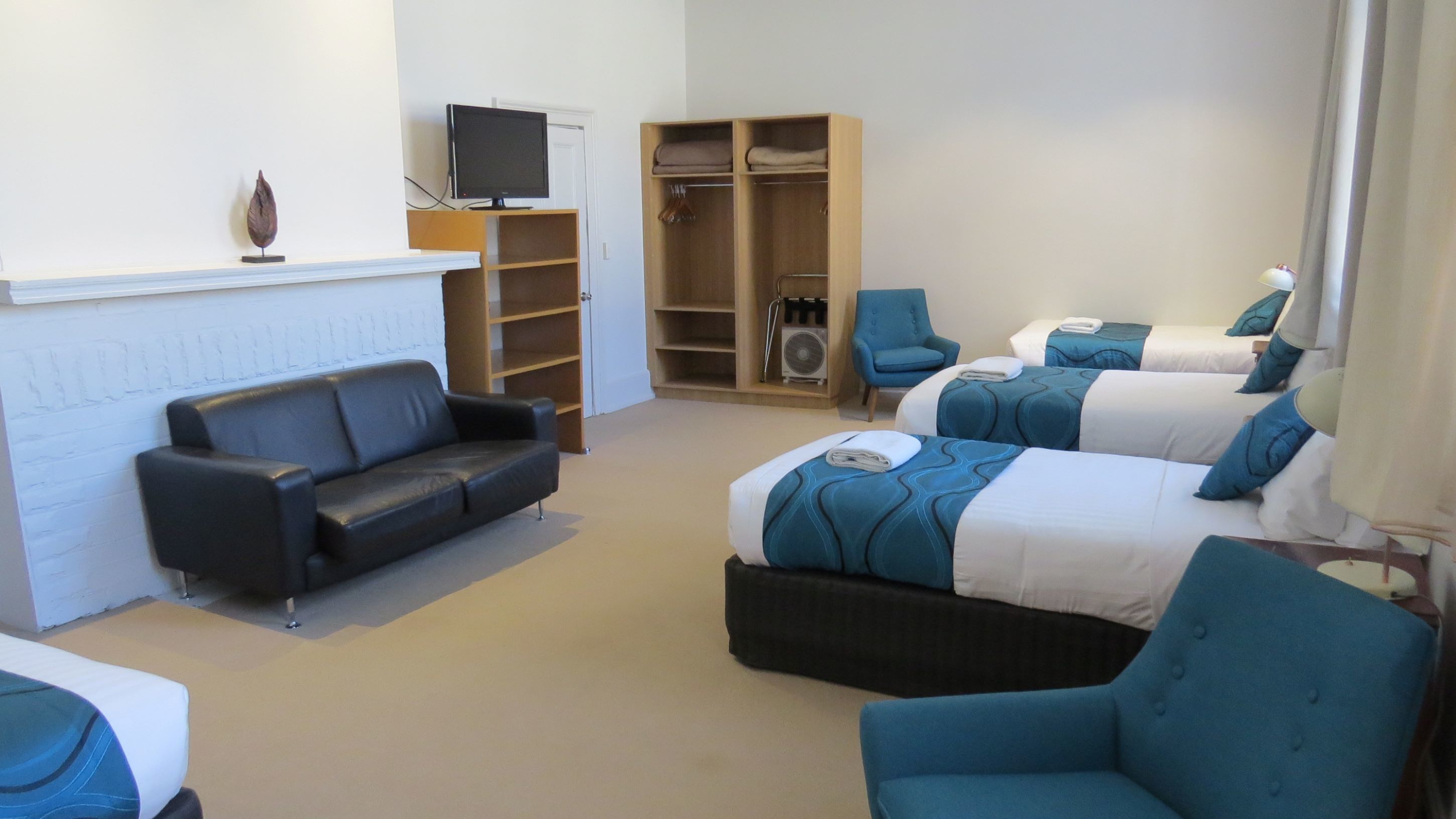 Une chambre d’hôtel avec un canapé, deux lits avec une parure de lit assortie, bleue et blanche, une télévision, une armoire et une petite table.