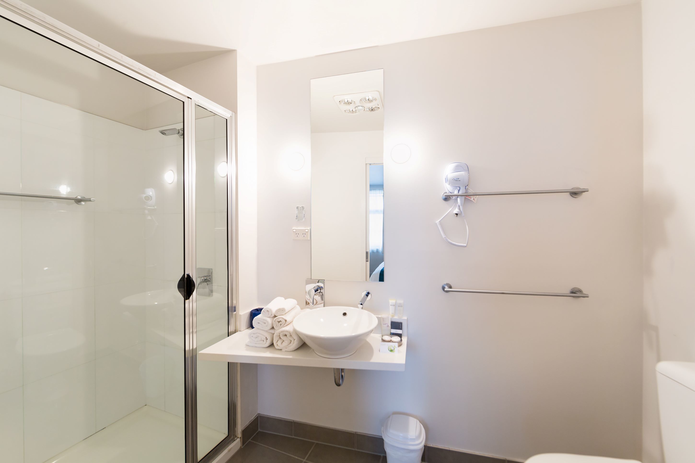 Een moderne badkamer met een douchecabine van glas, een witte wastafel met spiegel erboven en een handdoekrek.