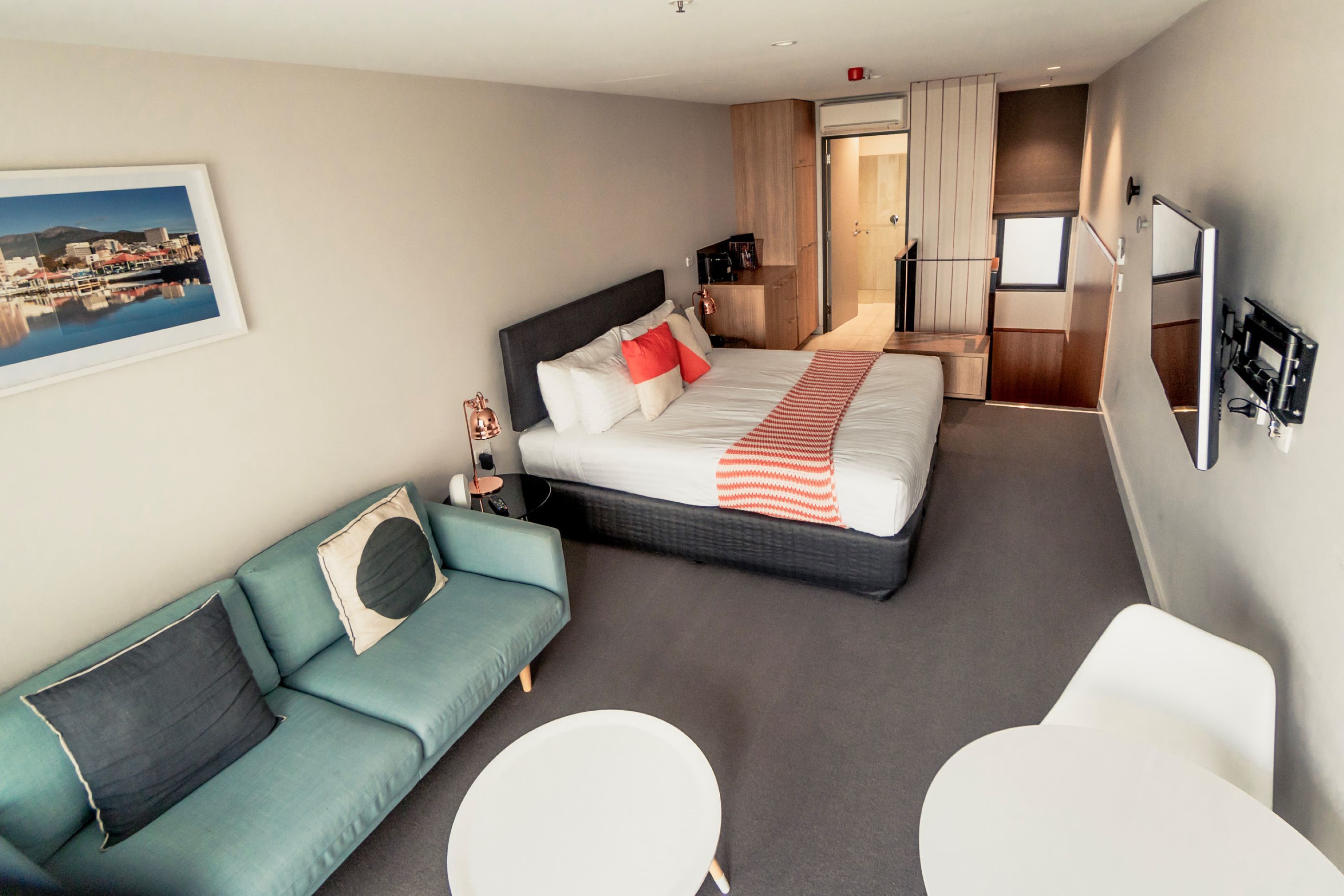 Una habitación de hotel moderna con una cama, un sofá, una mesita y un televisor.