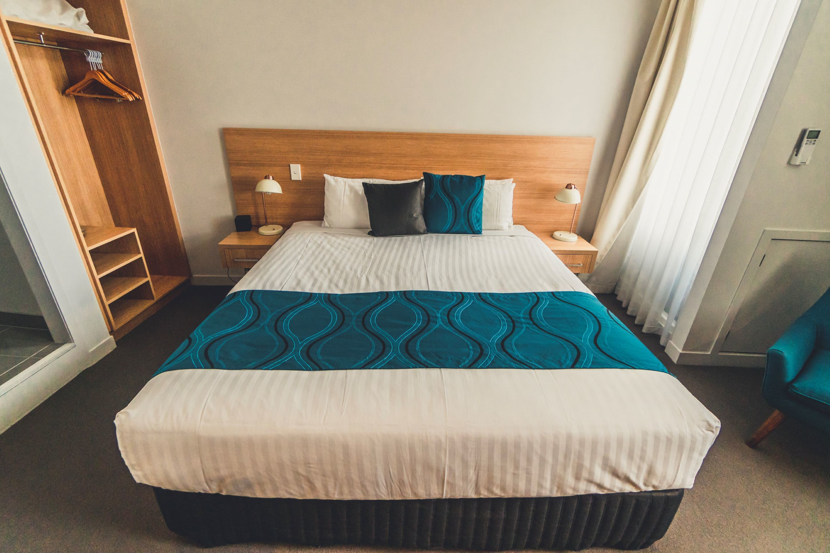 A hotel room with a large bed, a wooden headboard, a bedside table with a lamp, and a wardrobe.