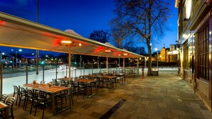 An outdoor dining area with tables and chairs, a covered walkway, and a view of the street. - Customs House Hotel (Hobart)