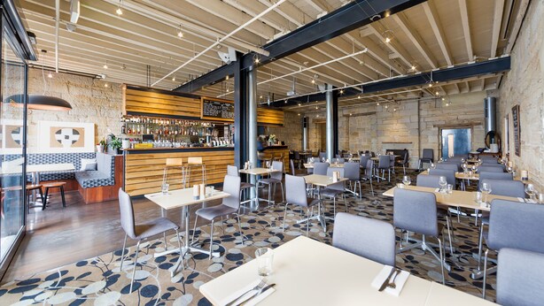 A spacious restaurant with high ceilings, exposed beams, and a bar area. Tables are arranged for dining, and the floor features a patterned carpet. - Customs House Hotel (Hobart)