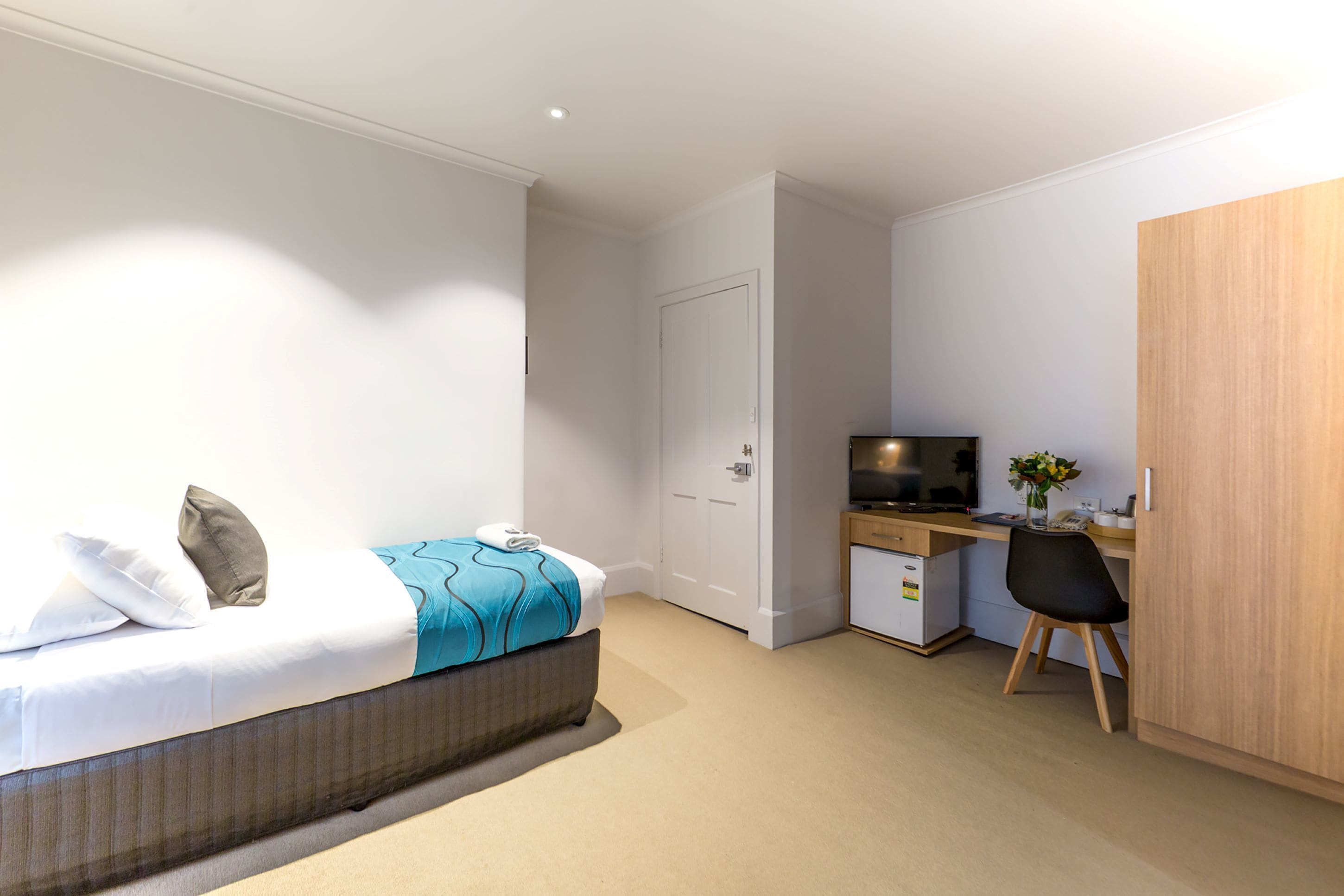 A modern hotel room with a bed, a desk, a television, and a wardrobe.