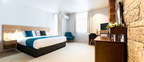 A hotel room with a large bed, a desk, a chair, and a TV.