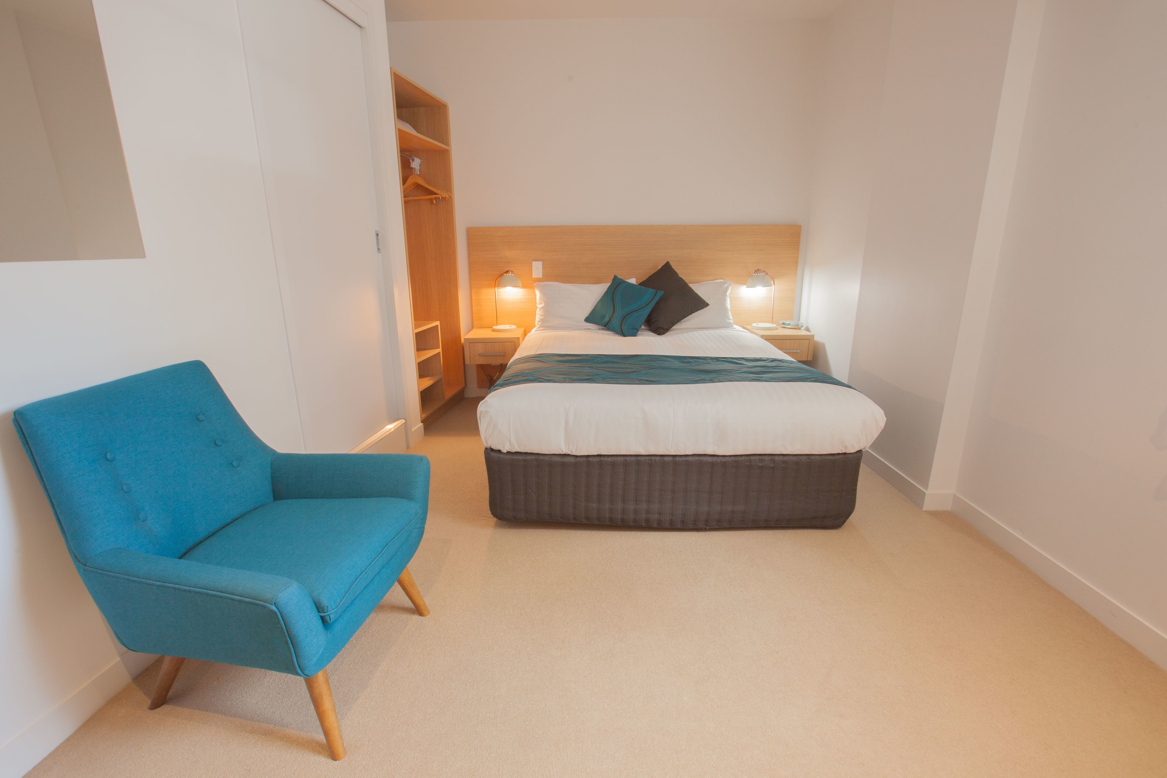 A bedroom with a bed, a blue chair, a nightstand, and a wardrobe.