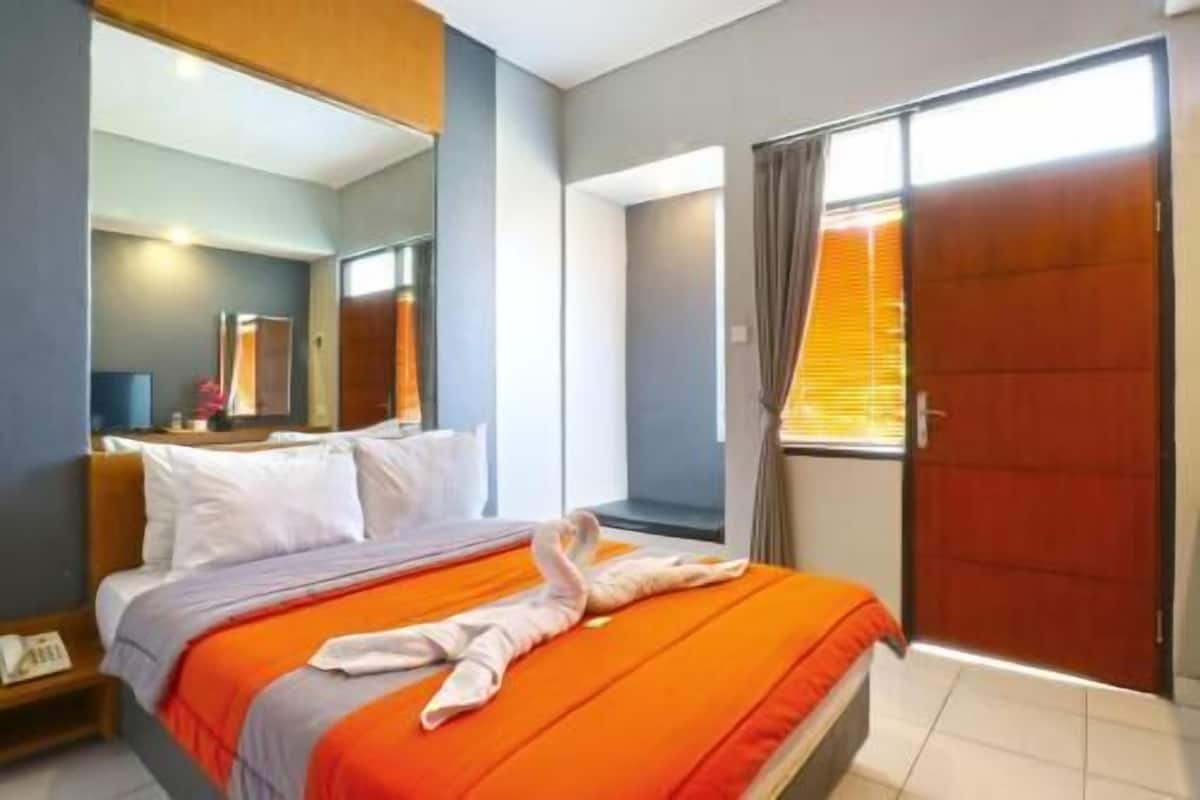 A hotel room with a bed, a mirror, a window with curtains, and a door.