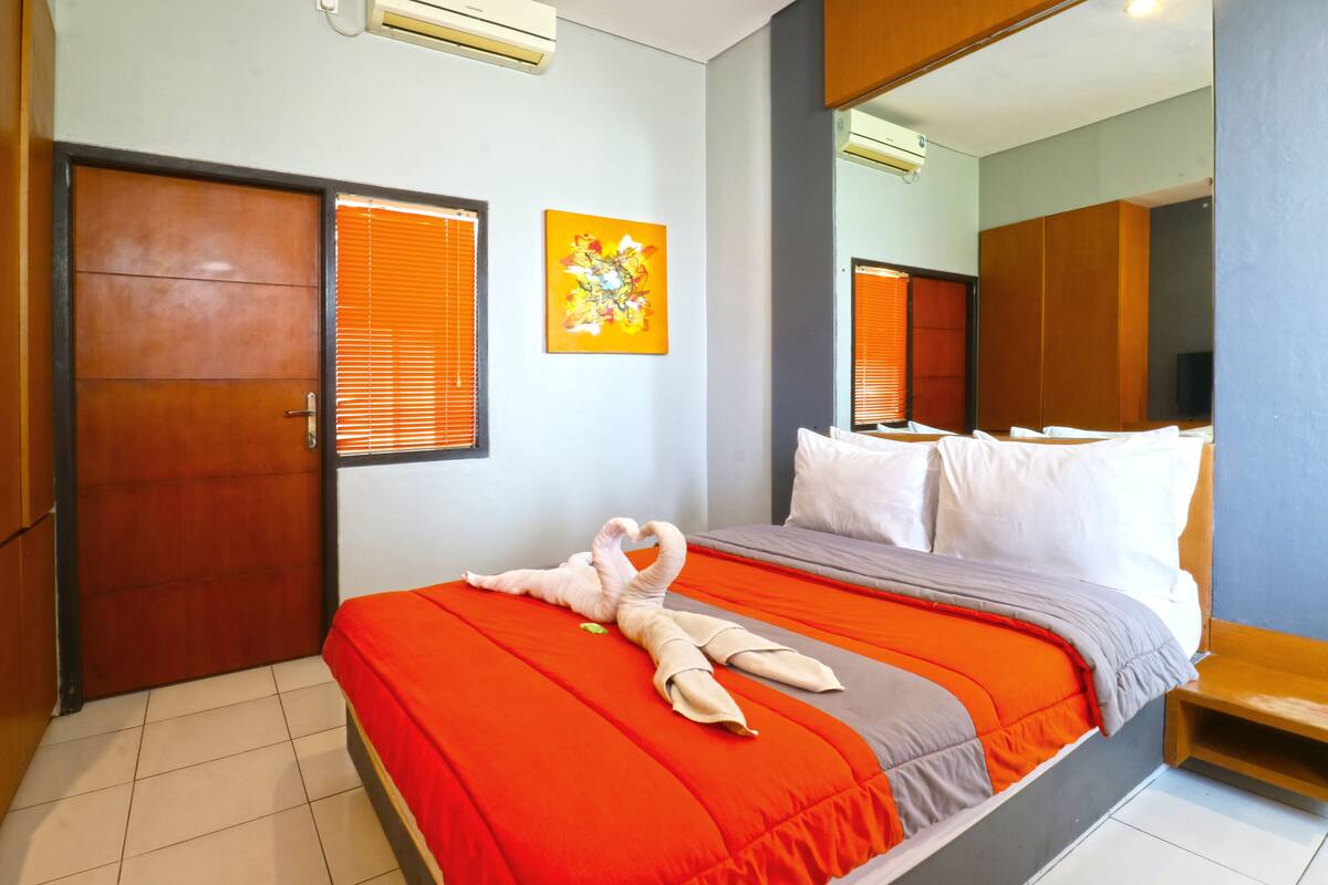 A hotel room with a bed, a mirror, a door, and a window.