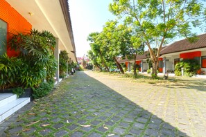 A paved pathway flanked by buildings with red and white facades, surrounded by greenery and trees. - Sayang Residence 2 (Denpasar)