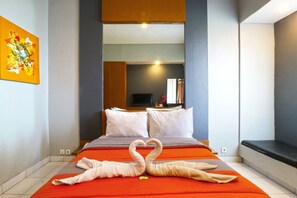 Et hotelværelse med en seng, puder, et fjernsyn og et billede på væggen.