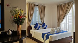 A hotel room with a bed, a desk with a kettle, a vase of flowers, and curtains. - Jun Yue Hotel (Phnom Penh)