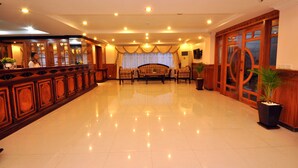 A spacious lobby with a polished floor, a reception desk, a seating area with a sofa, and a large wooden door. - Jun Yue Hotel (Phnom Penh)