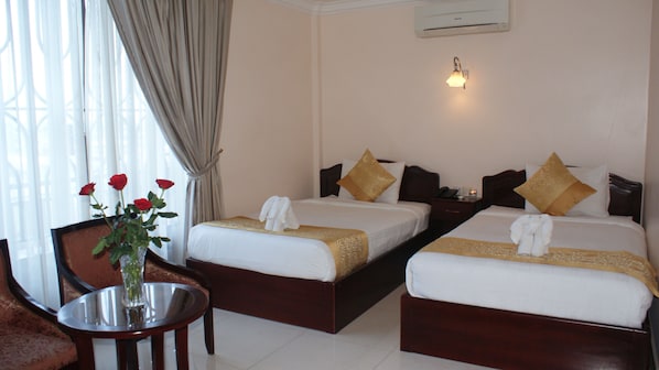 A hotel room with two beds, a nightstand, a table with a vase of flowers, and a window with curtains. - Jun Yue Hotel (Phnom Penh)