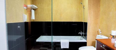 A modern bathroom with a glass shower enclosure, a white bathtub, and a separate toilet area.