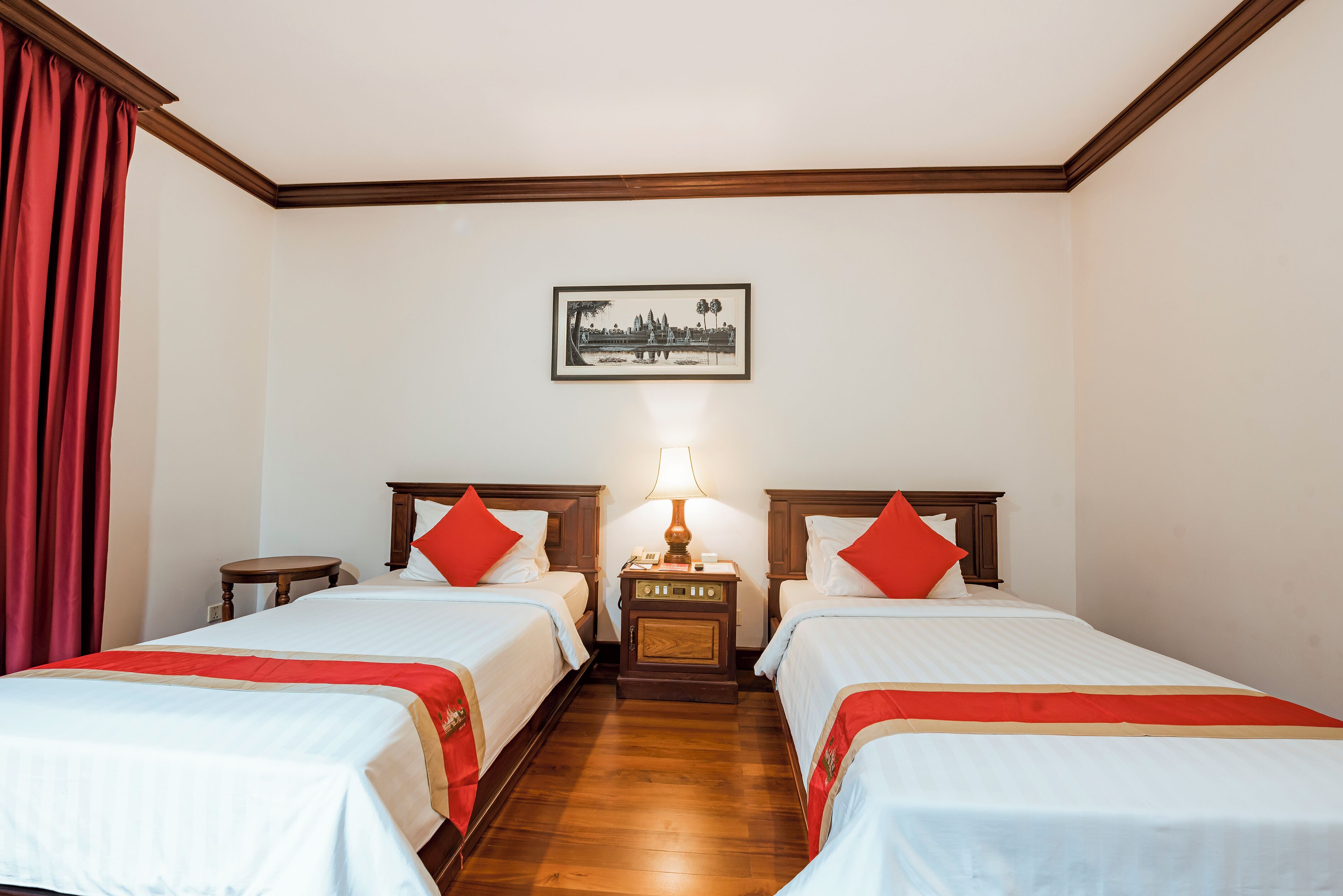Habitación de hotel con dos camas, una mesita de noche con lámpara y un cuadro en la pared.