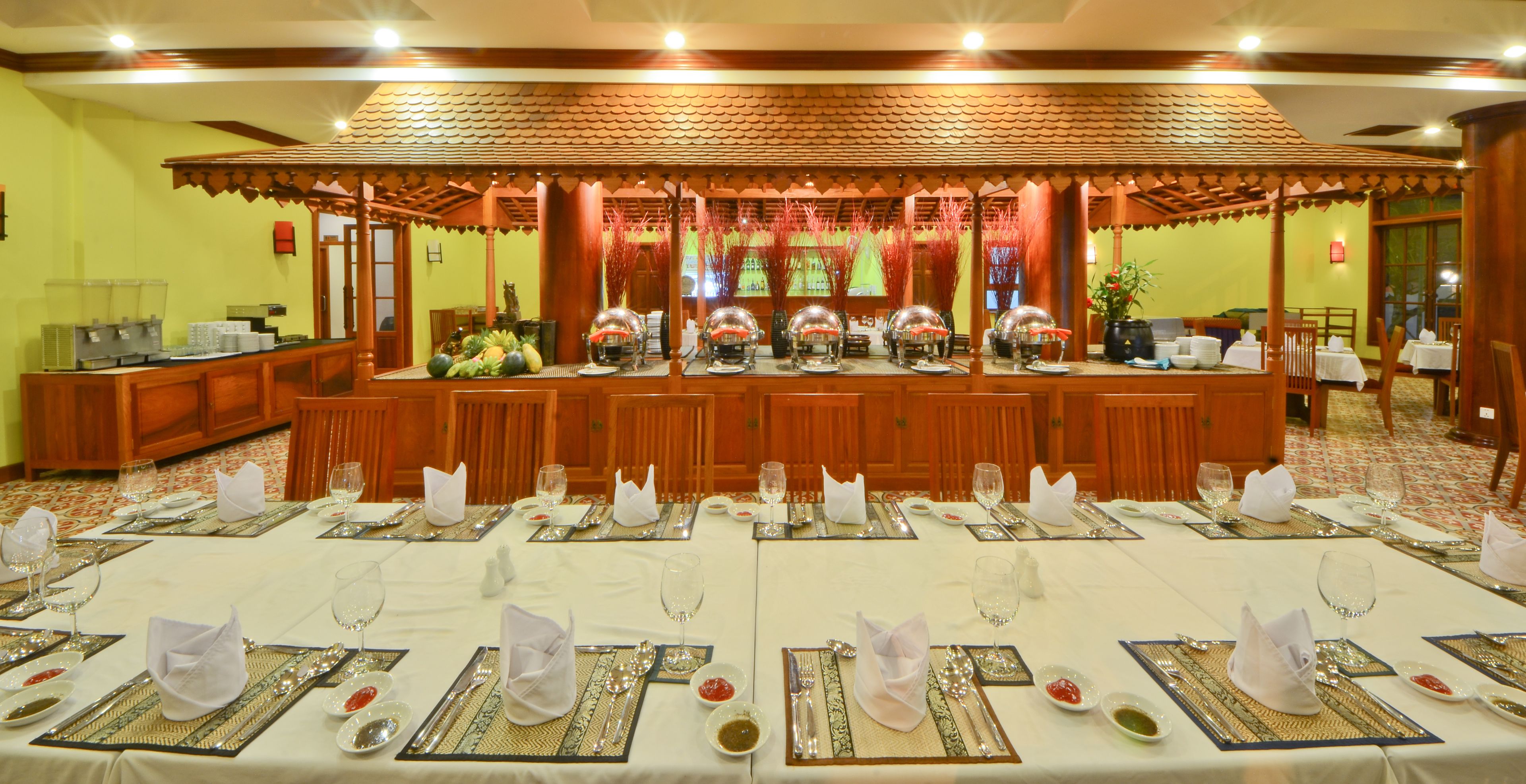 Un salón de banquetes con largas mesas dispuestas para un evento formal, un escenario central con elementos decorativos y un estilo arquitectónico tradicional.