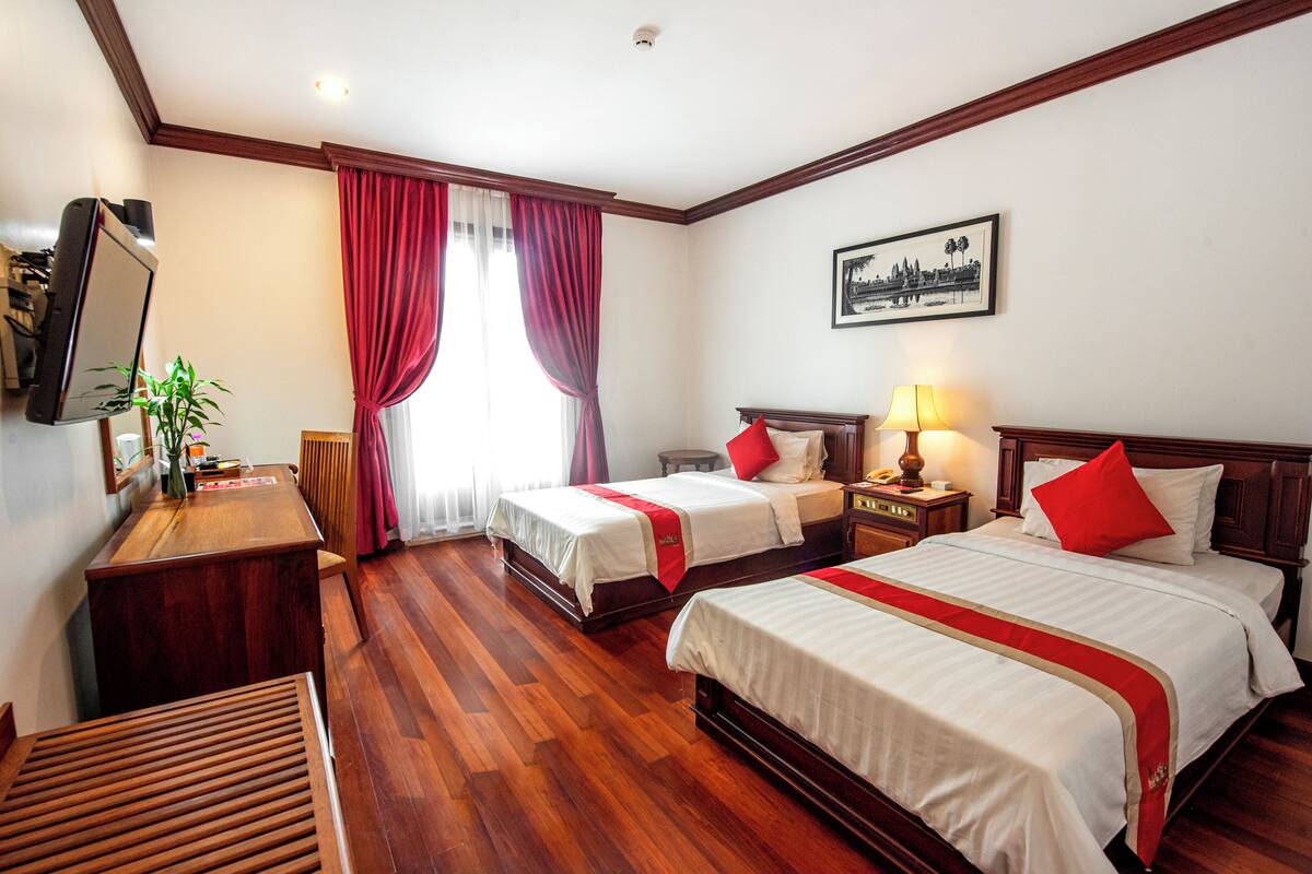 Quarto de hotel com duas camas, uma escrivaninha, uma cadeira, uma televisão e uma janela com cortinas.