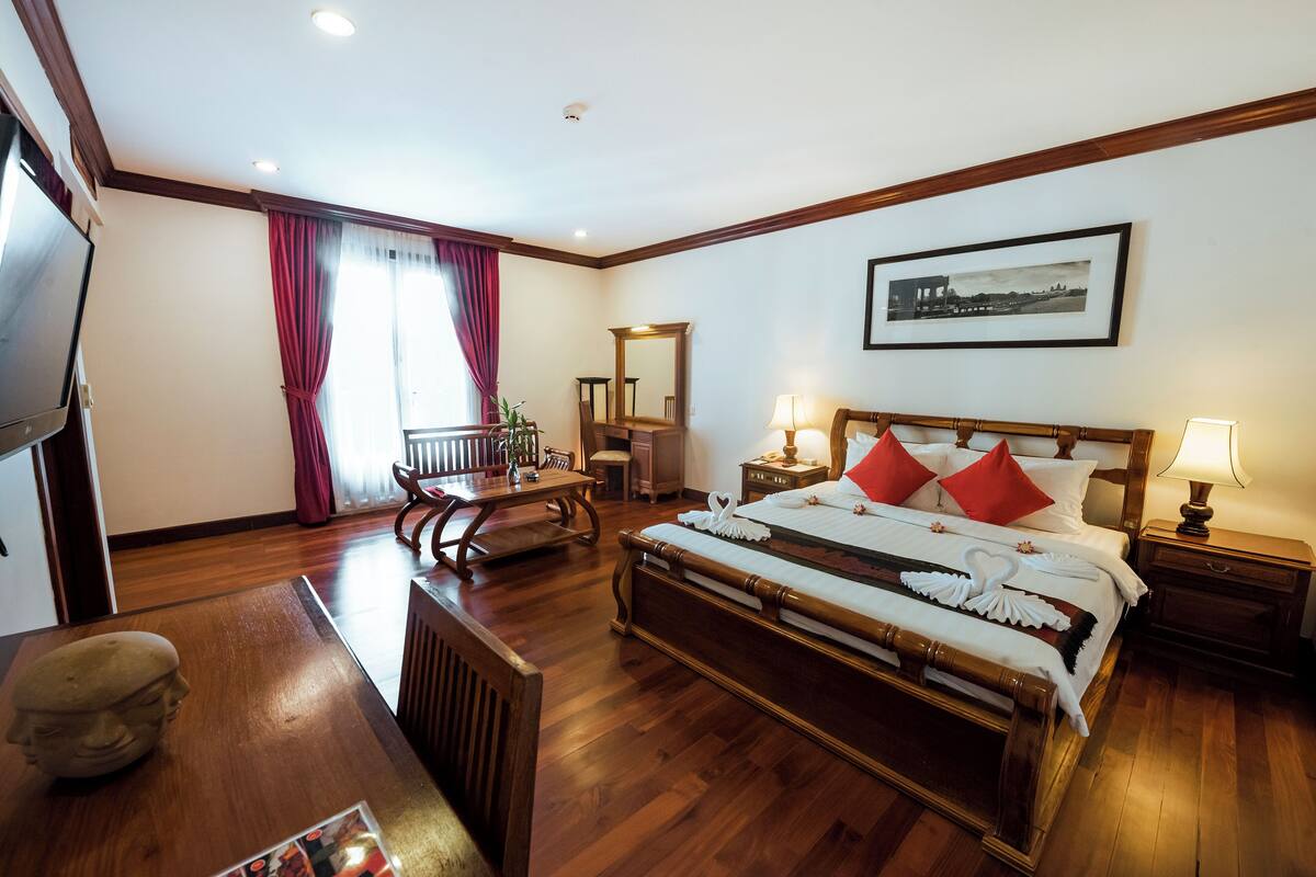 Quarto de hotel com uma cama de madeira, uma escrivaninha, uma cadeira, uma televisão e um quadro na parede.
