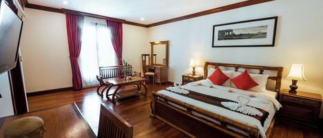 Habitación de hotel con cama de madera, un escritorio, una silla, un televisor y un cuadro en la pared.