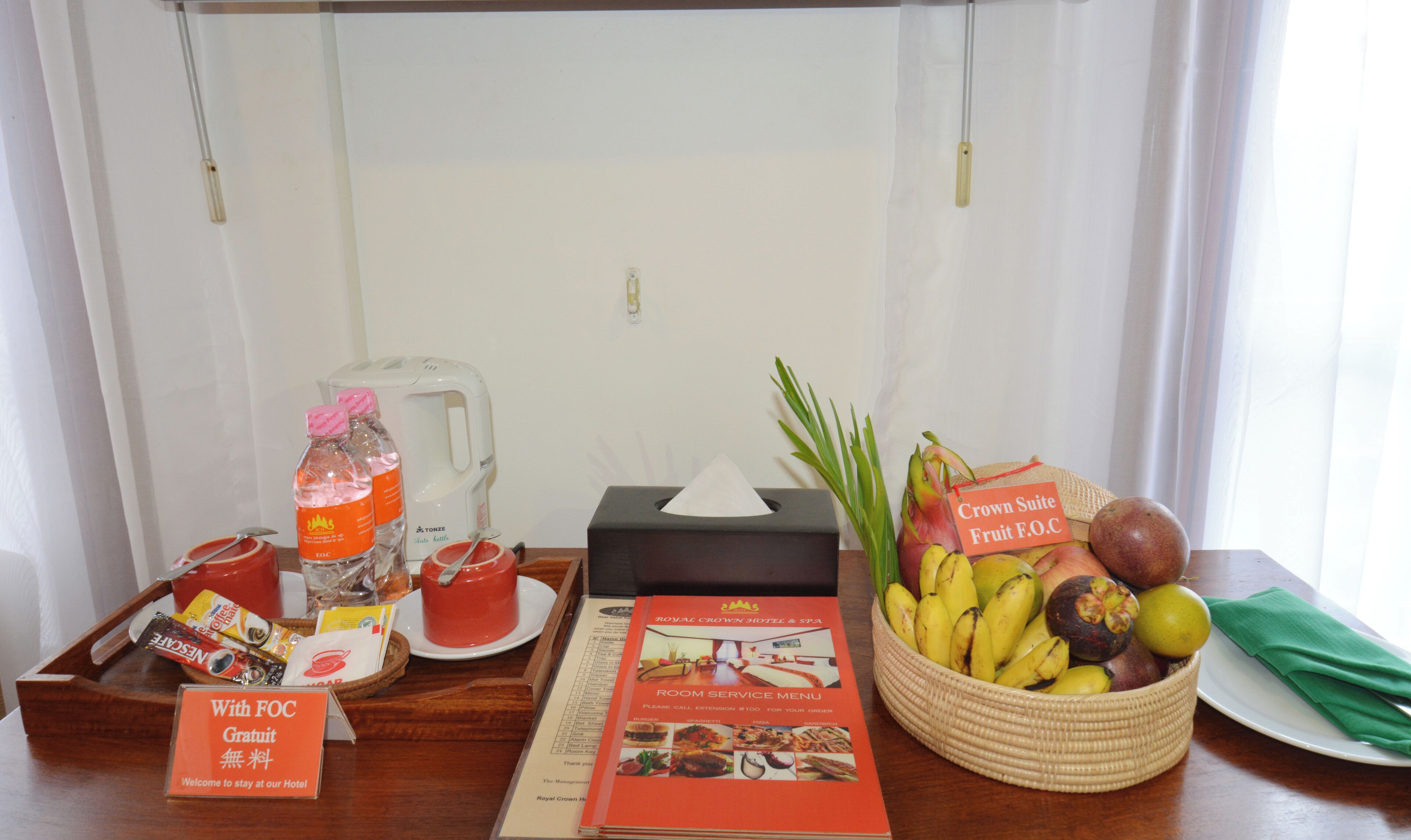 A hotel room's reception area with a fruit basket, a menu, a coffee maker, and a sign indicating complimentary fruit.