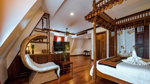 Un dormitorio con cama con dosel, una silla de mimbre, un televisor y un escritorio con una planta.