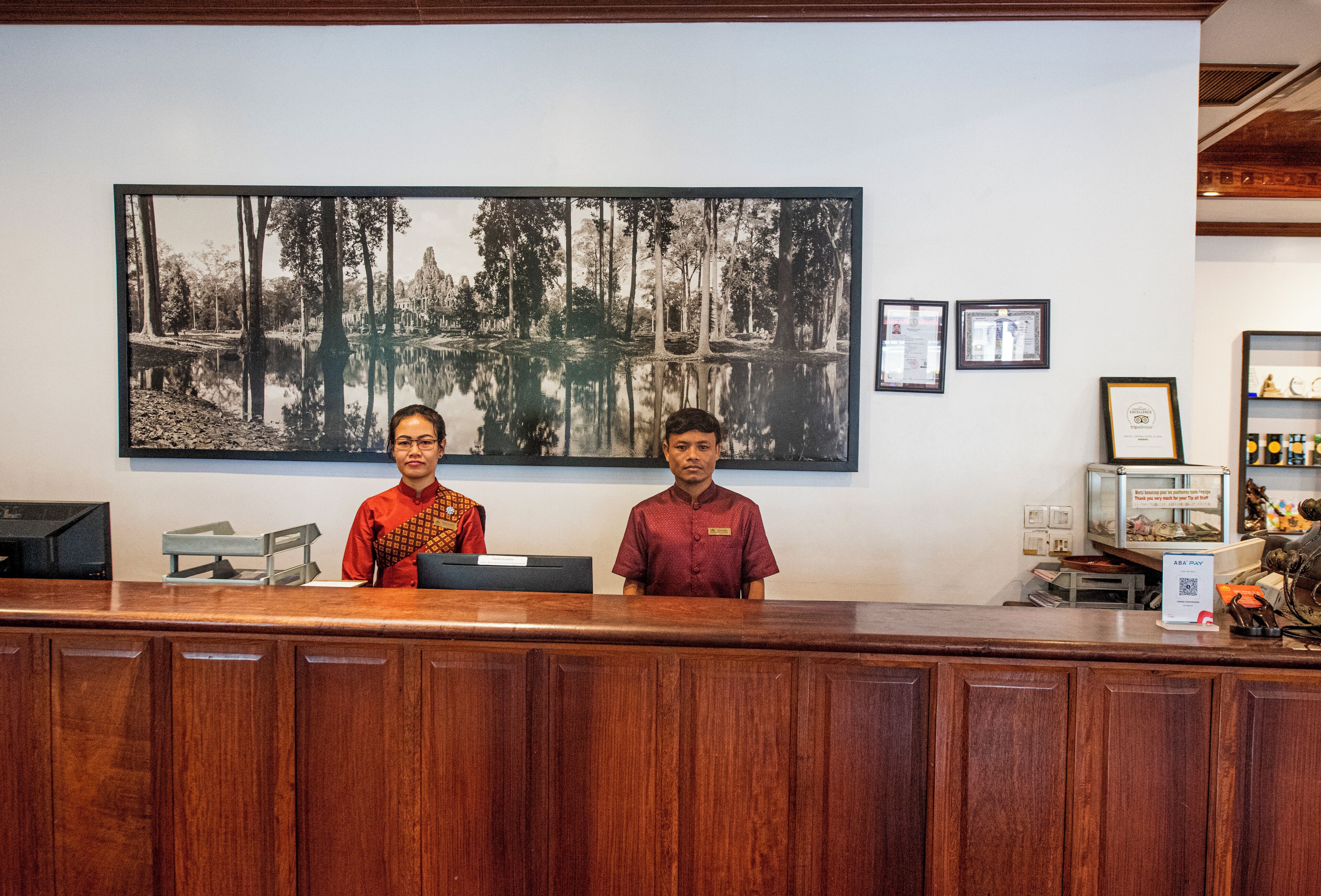A reception desk with two staff members, a large framed photograph of a forest on the wall, and a few framed awards.