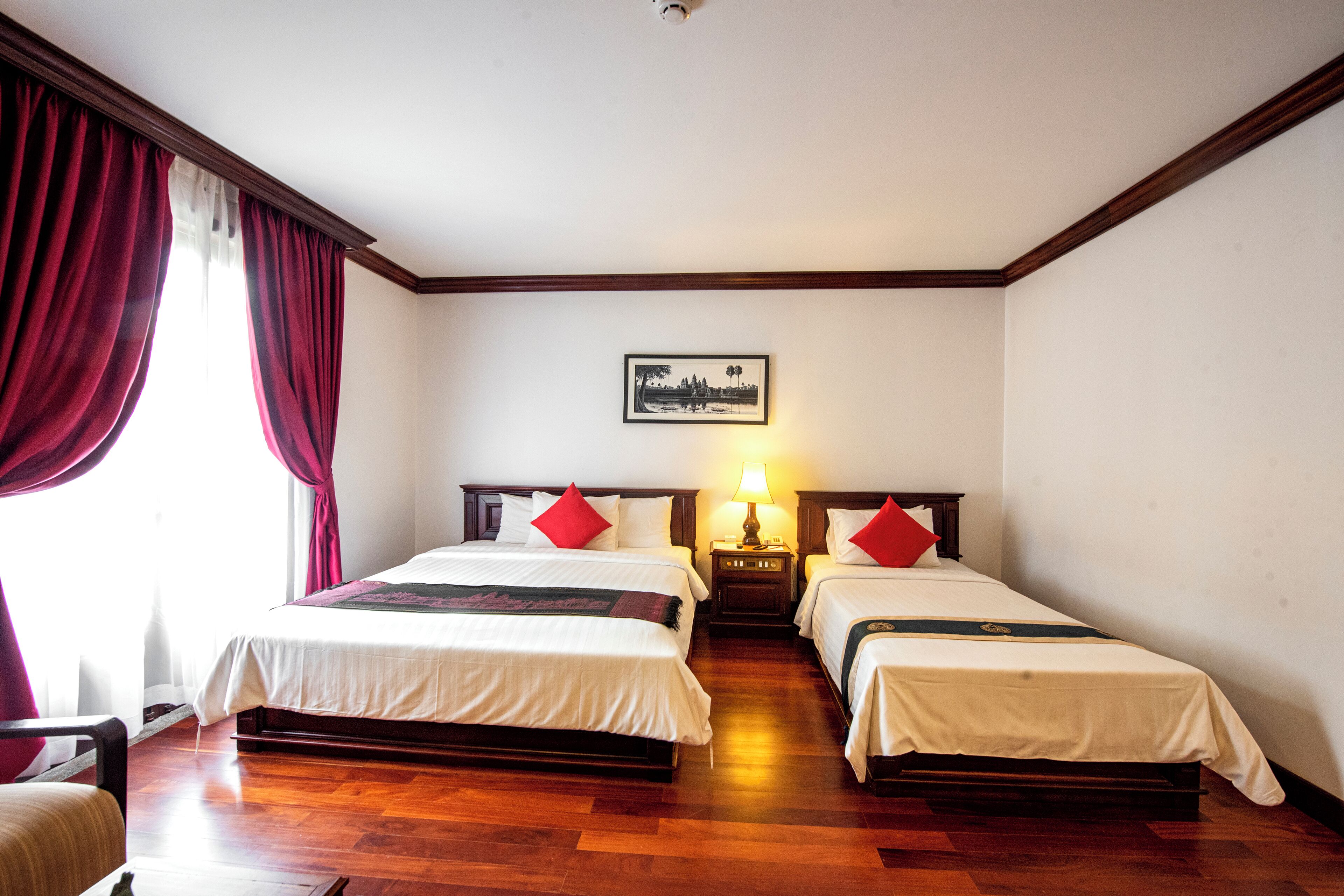 Habitación de hotel con dos camas, piso de madera, una mesita de noche con lámpara y un cuadro enmarcado en la pared.