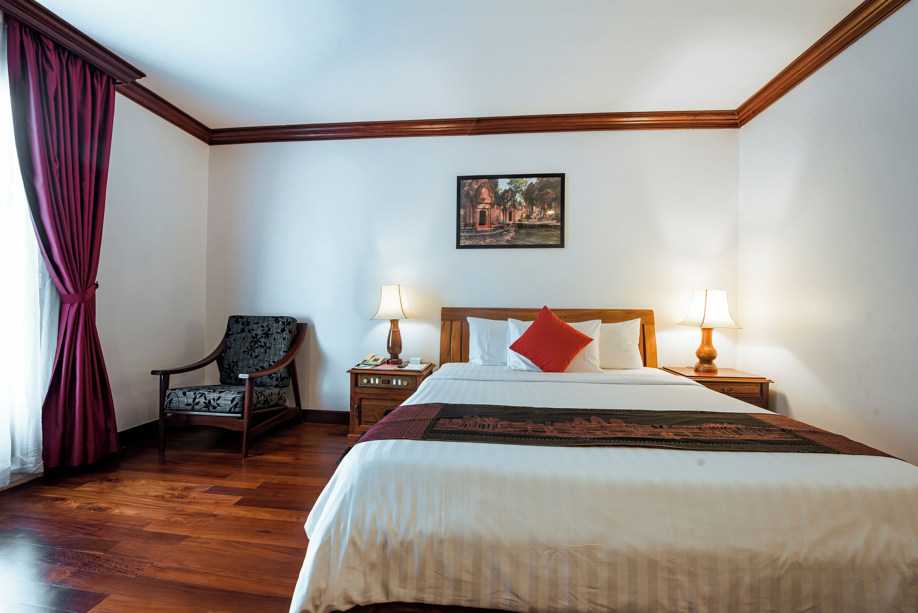 Habitación de hotel ordenada con una cama grande, dos mesitas de noche con lámparas, una silla e imagen enmarcada en la pared.