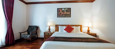 Habitación de hotel ordenada con una cama grande, dos mesitas de noche con lámparas, una silla e imagen enmarcada en la pared.