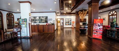A spacious lobby with a wooden floor, a reception desk, and a chandelier.