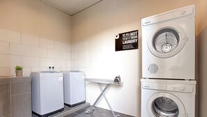 A laundry room with two washing machines, a drying machine, and an ironing board. - the youniQ Hotel (Sepang)