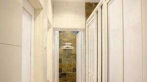 A narrow hallway with white doors on both sides, a tiled floor, and a stone wall at the end. - the youniQ Hotel (Sepang)