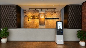 A reception area with a brick wall, a sign reading 'The Young Hotel,' and a digital check-in kiosk. - the youniQ Hotel (Sepang)