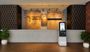 A reception area with a brick wall, a sign reading 'The Young Hotel,' and a digital check-in kiosk. - the youniQ Hotel (Sepang)