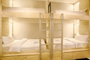 Ein Schlafraum mit Etagenbett, einer Stehleiter, weißer Bettwäsche und Holzwänden.